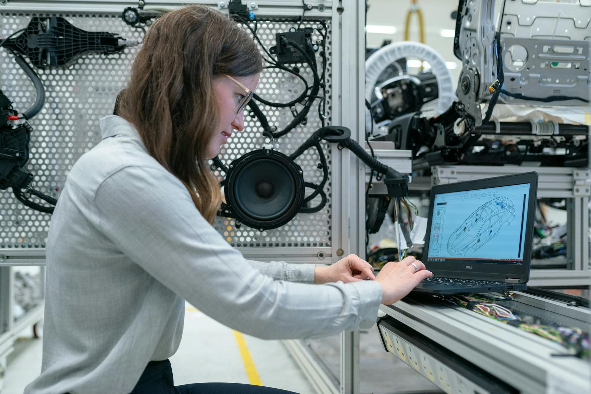 A young woman in an automotive systems lab working on vehicle CAD with hardware rigs behind her