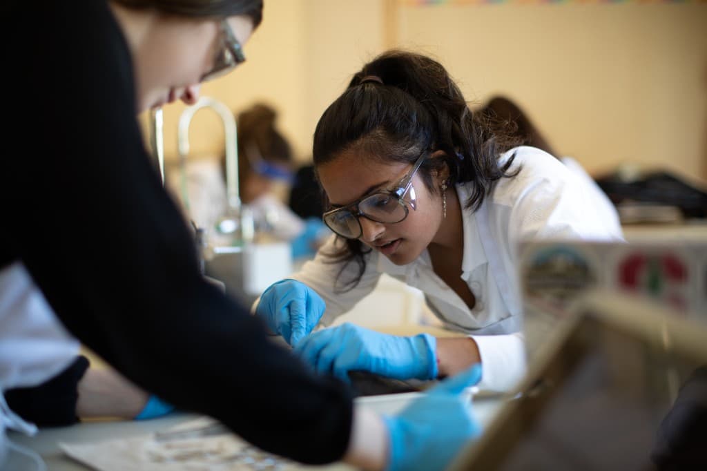 High school students in a biomedical lab wearing safety goggles and gloves during hands-on practice
